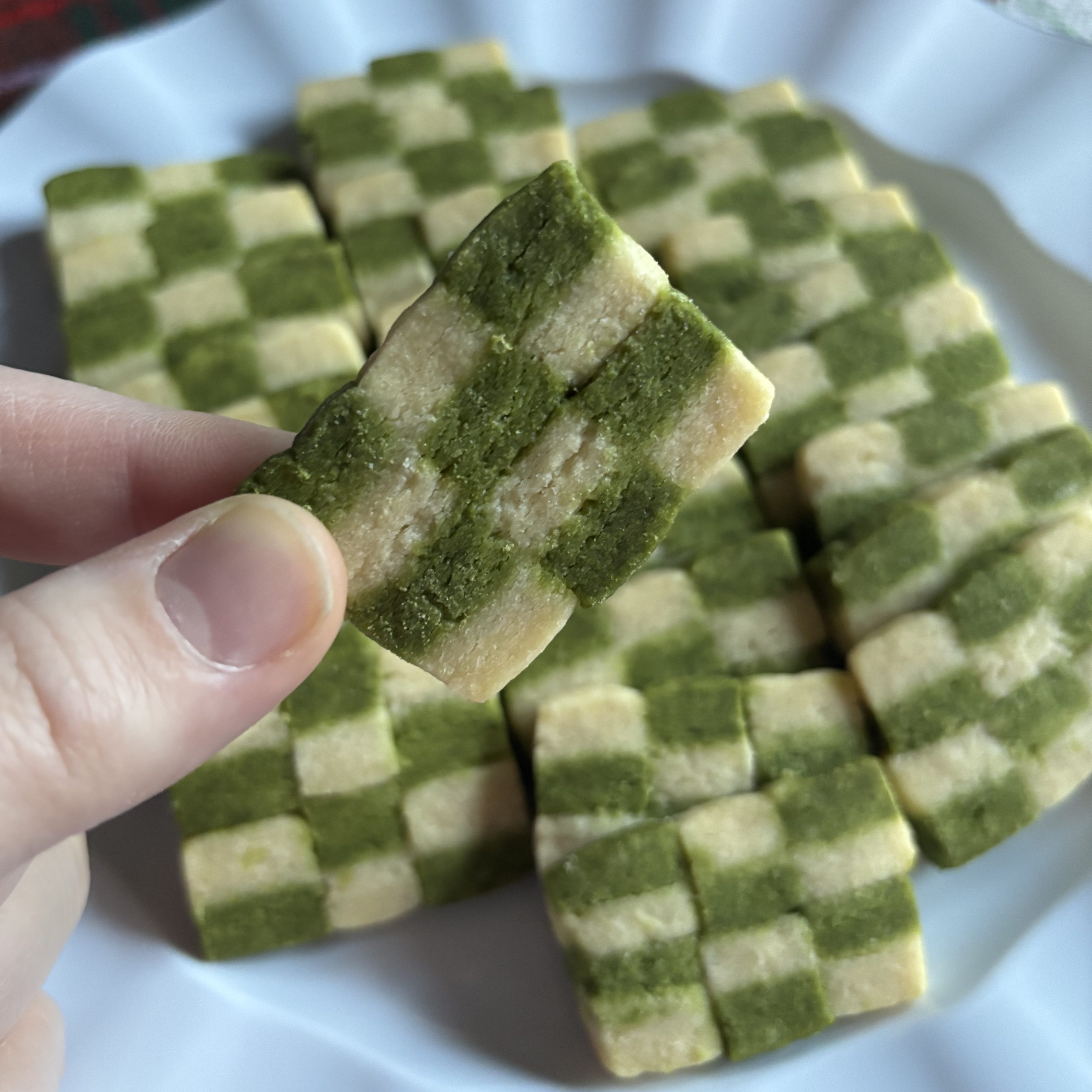 A plate of matcha checkerboard cookies. One cookie is held up in front of the rest.