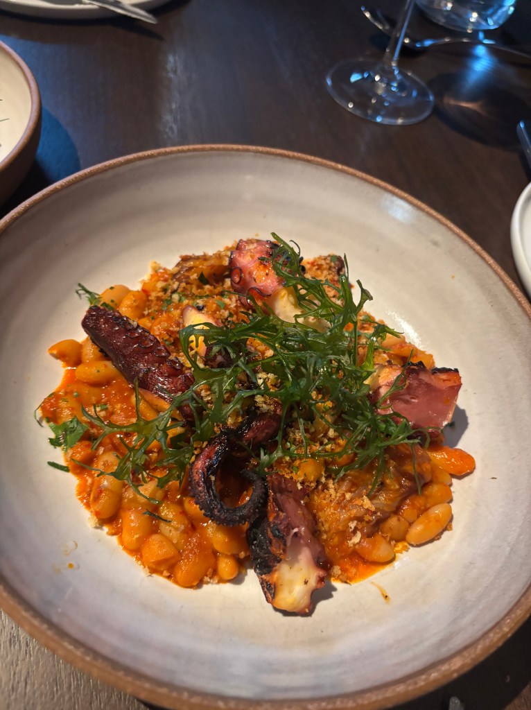 Grilled octopus on white beans in a red sauce.