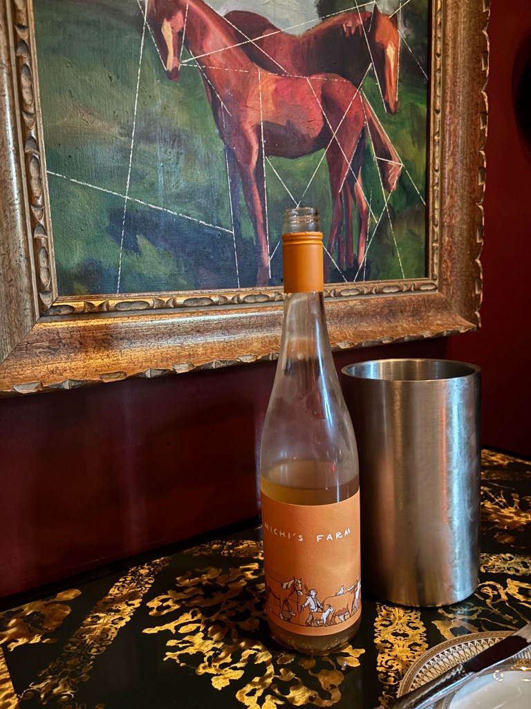 A picture of a bottle of orange wine in front of a geometric horse portrait.