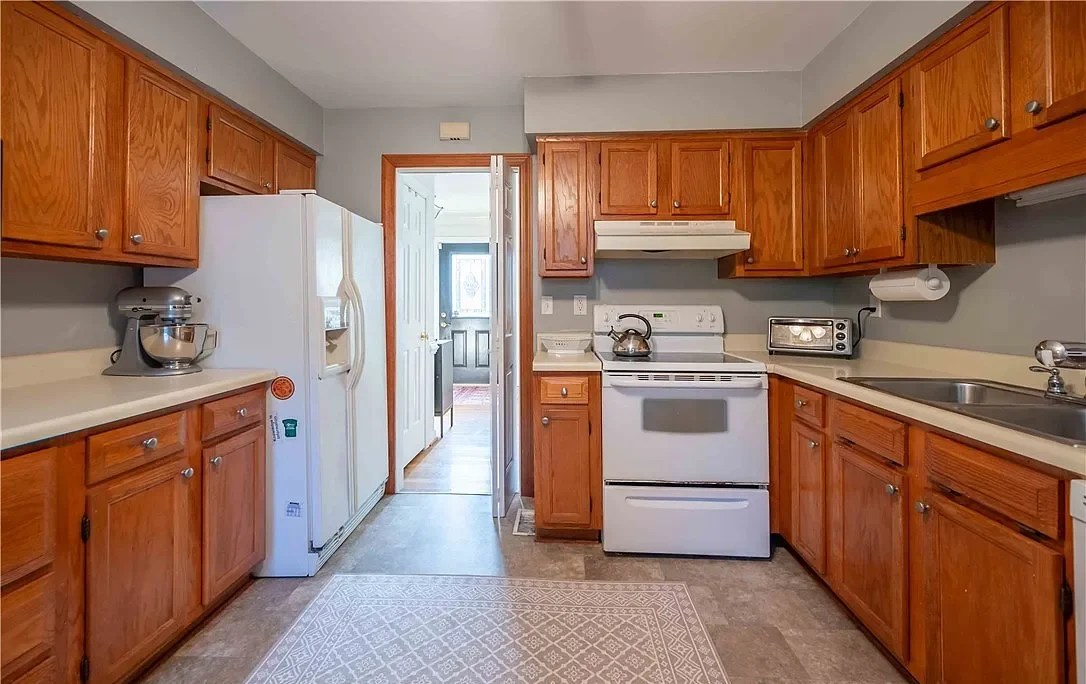 A small kitchen with honey oak cabinets and old appliances.