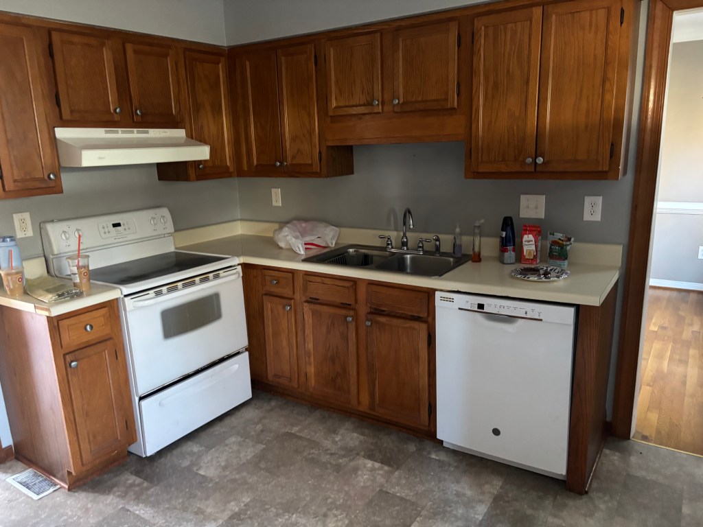 A picture of an old kitchen with honey oak cabinets taken from an angle that focuses on half the kitchen.