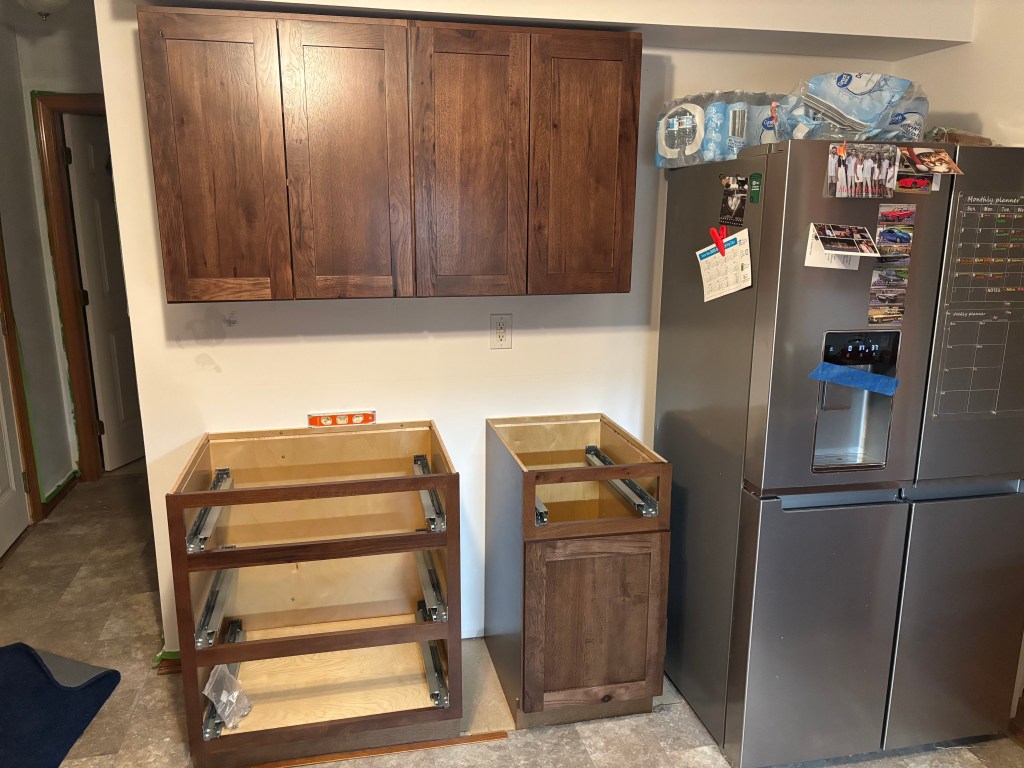 Part of a kitchen with a new fridge and dark wood cabinets put up.