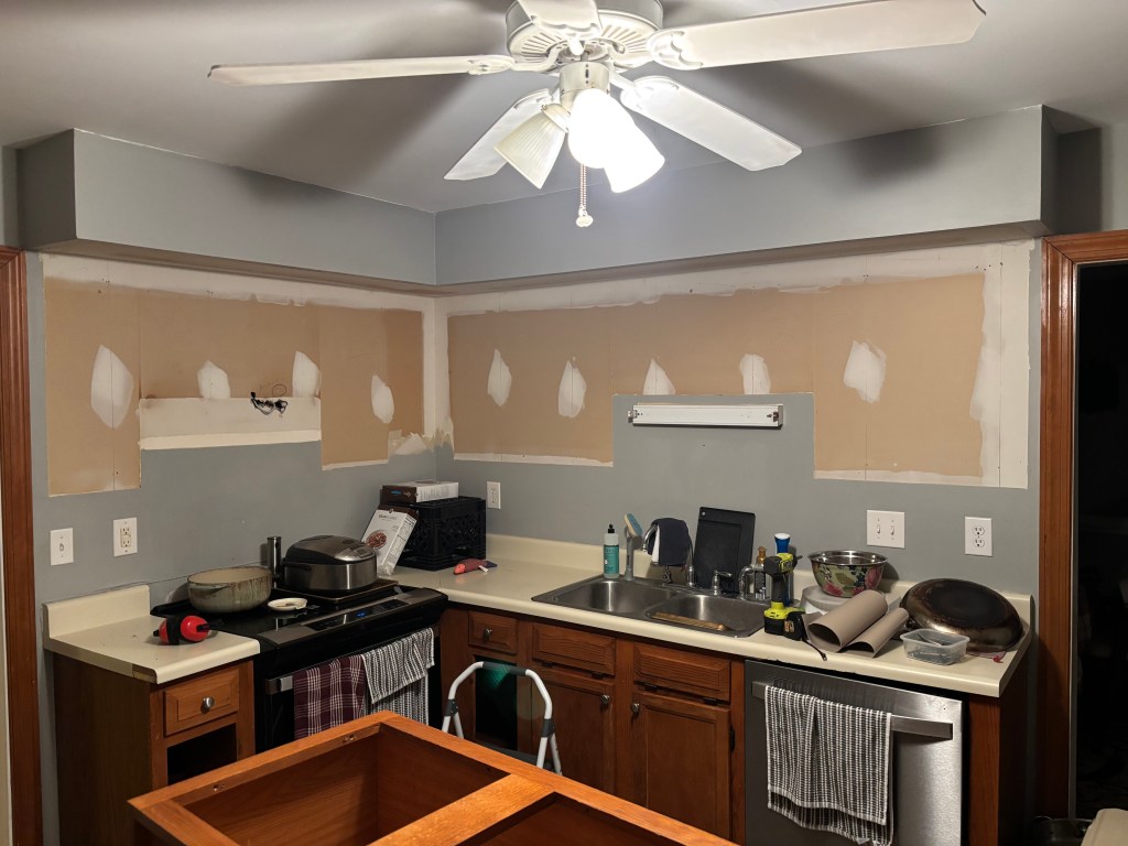 Part of a kitchen with top cabinets missing and old honey oak cabinets still in place on the bottom.