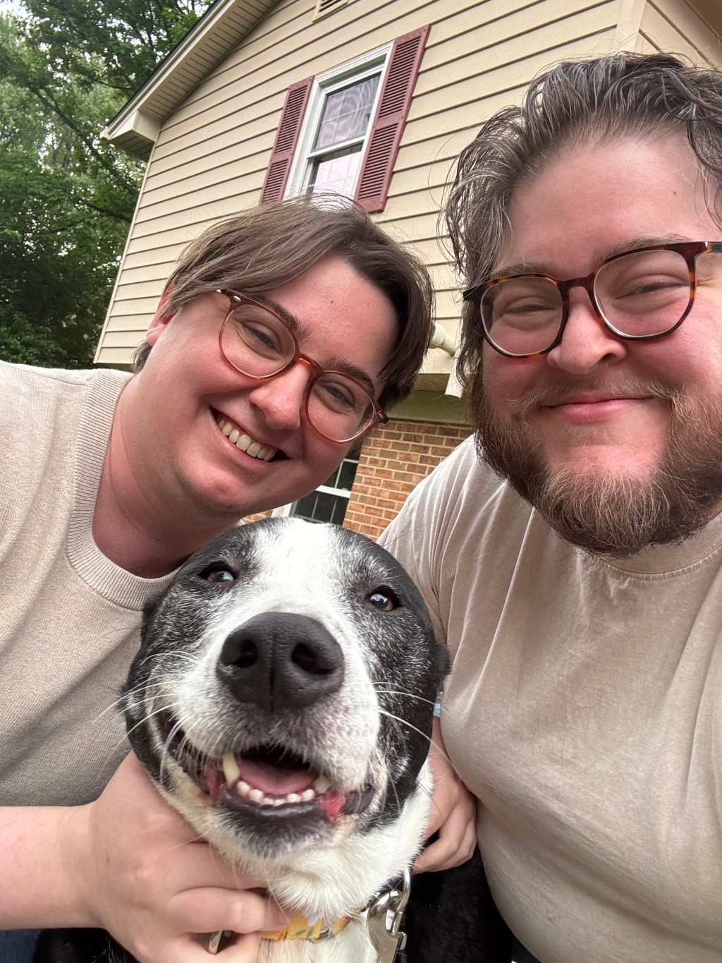 A picture of two white men with their black and white pitbull mix. The dog is making a silly face.