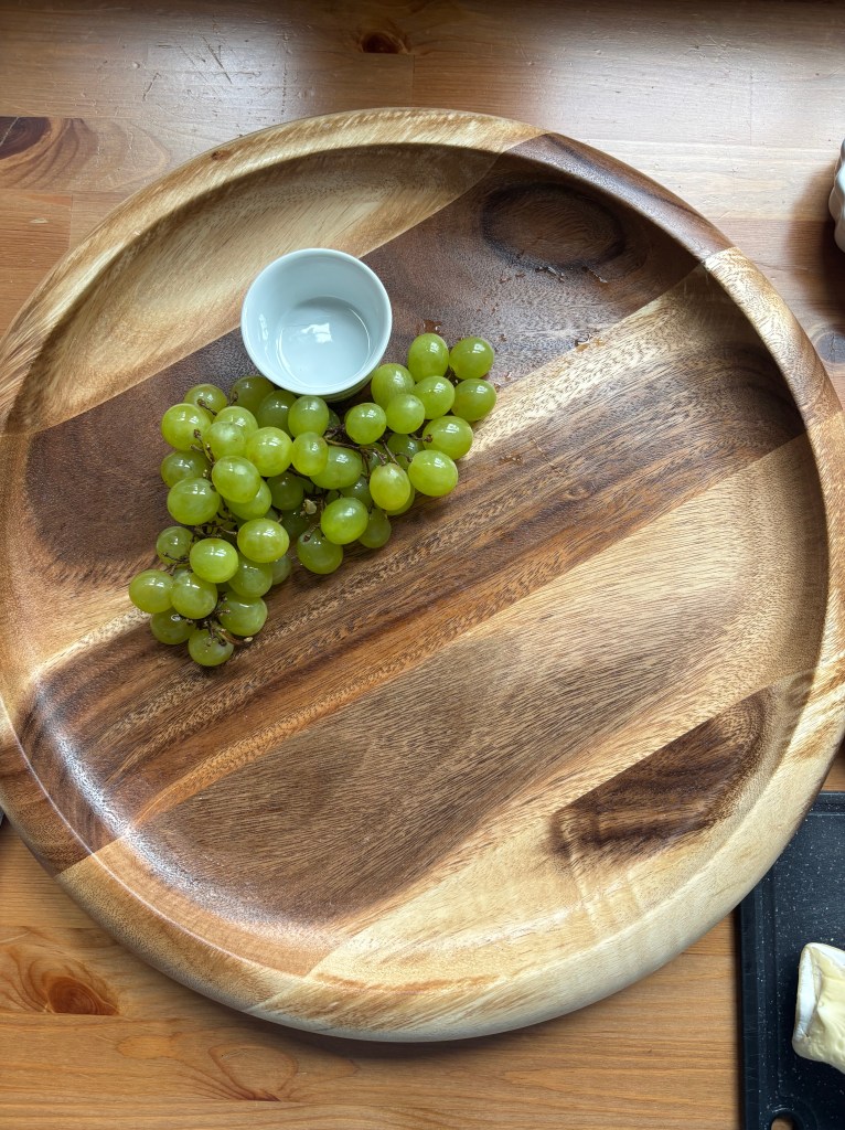 An empty cheese board except for a row of grapes.
