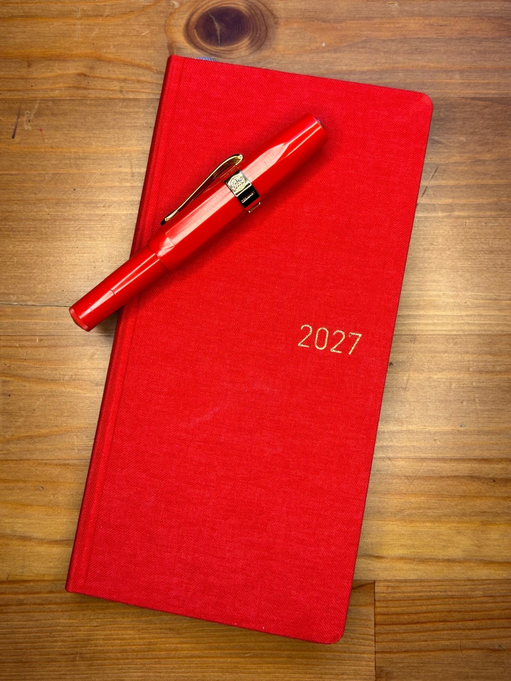 A poppy red hobonichi weekly planner with a Kaweco sport fountain pen on it (also in red).